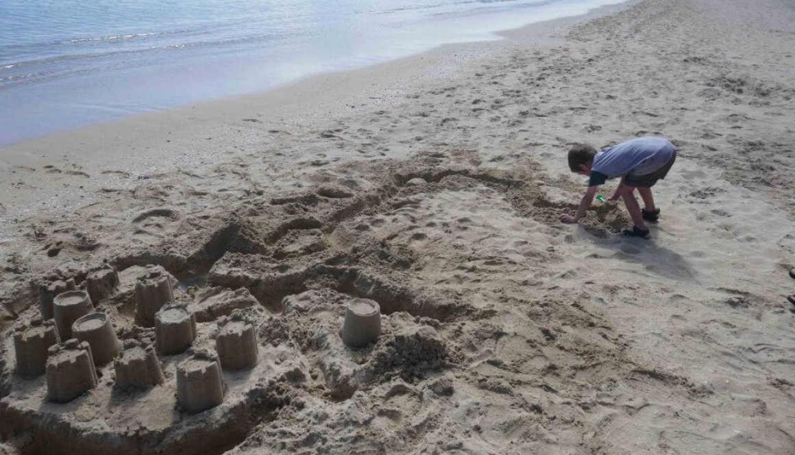 why being bored is good for kids. Boy building sandcastles at the beach