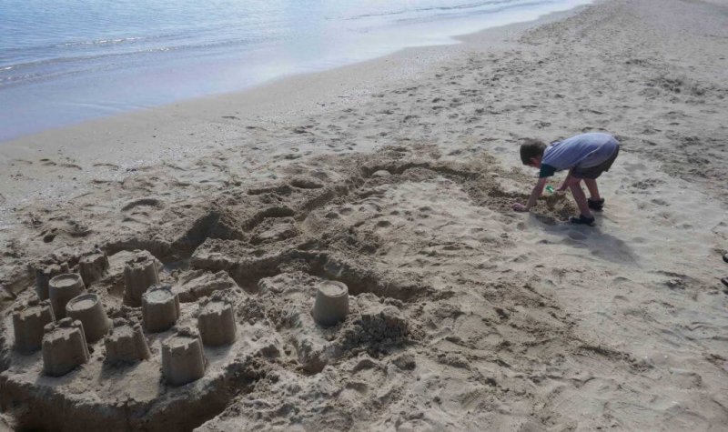 why being bored is good for kids. Boy building sandcastles at the beach
